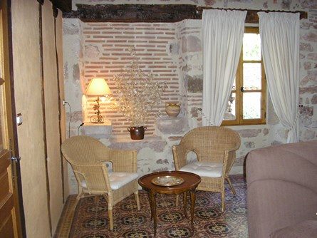 Le-moulin-de-maraval-Cordes-sur-ciel-petit-salon-5 Coin salon chaleureux avec fauteuils en osier, canapé, télé. Mur de briques et pierre apparentes avec colombages ; carreaux de ciment