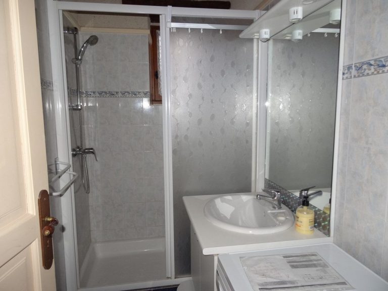 Salle de bain avec douche, lavabo et miroir. Cachet authentique avec pierres et poutres apparentes