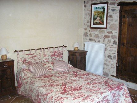 Le-moulin-de-maraval-cordes-sur-ciel-chambre-rouge-9 Chambre à ambiance rustique avec lit 140, mur en pierres et plâtre provençal teinté. Poutres bois au plafond.