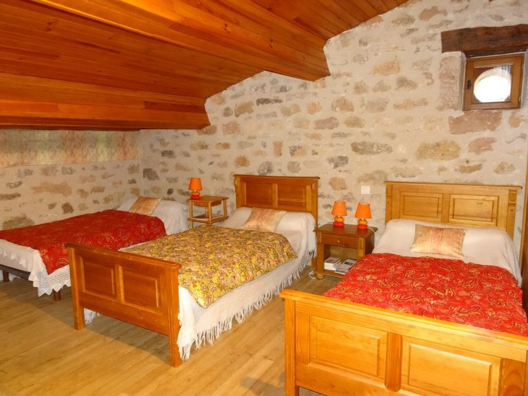 Chambre avec trois lits simples et murs en pierre, décor rustique et chaleureux.